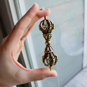 May include: A gold-coloured metal hand-held prayer wheel with intricate details and a pointed tip.