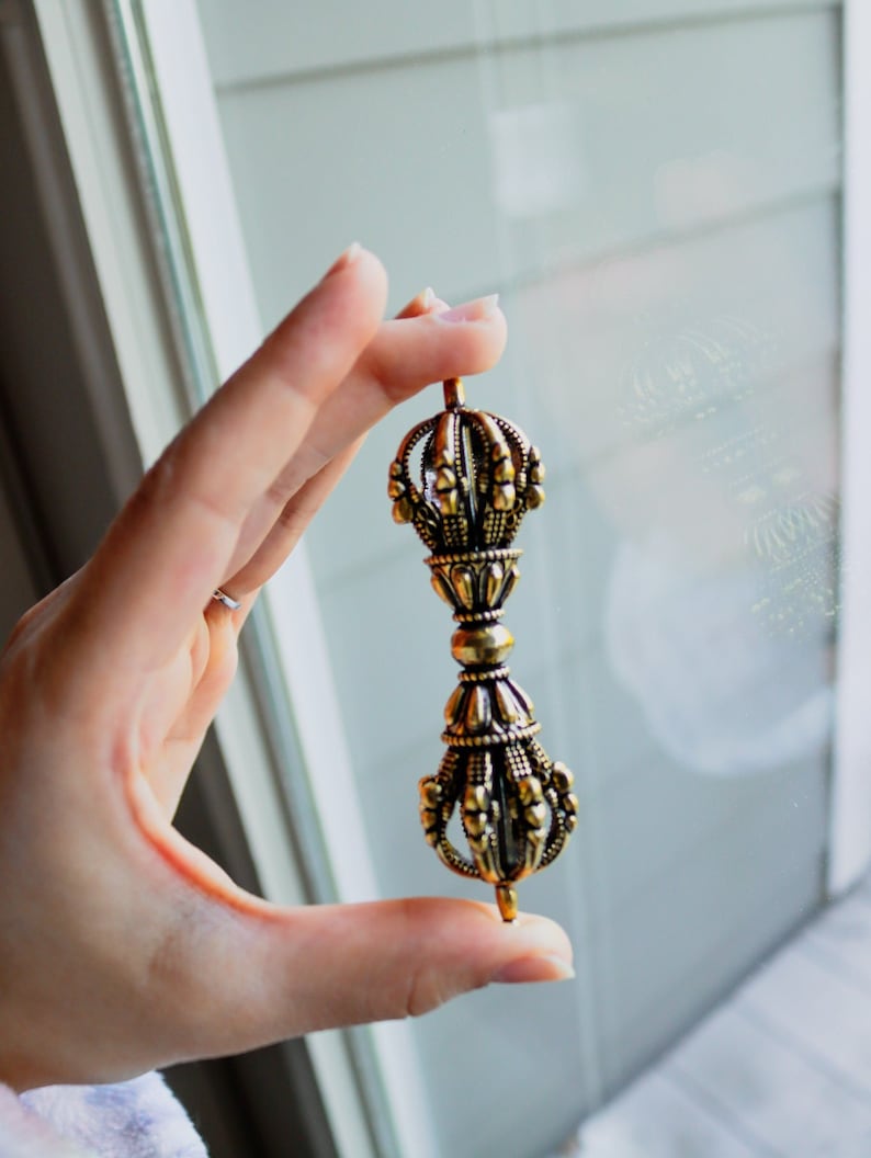 May include: A gold-colored metal hand-held prayer wheel with intricate details and a pointed tip.