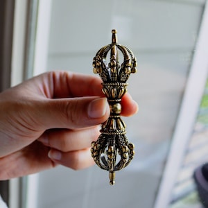 May include: A gold-colored metal hand-held prayer wheel with intricate details and a pointed tip.