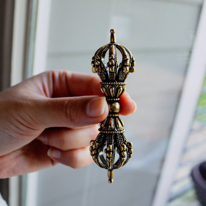 May include: A gold-colored metal hand-held prayer wheel with intricate details and a pointed tip.