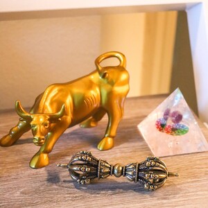 May include: A gold bull figurine, a clear crystal pyramid, and a brass prayer wheel with intricate details.