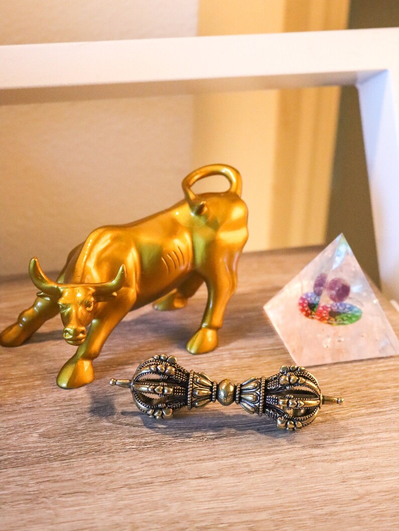 May include: A gold bull figurine, a clear crystal pyramid, and a brass prayer wheel with intricate details.