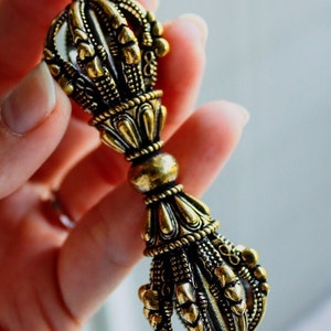 May include: A gold-colored metal hand-held prayer wheel with intricate details and a pointed tip.