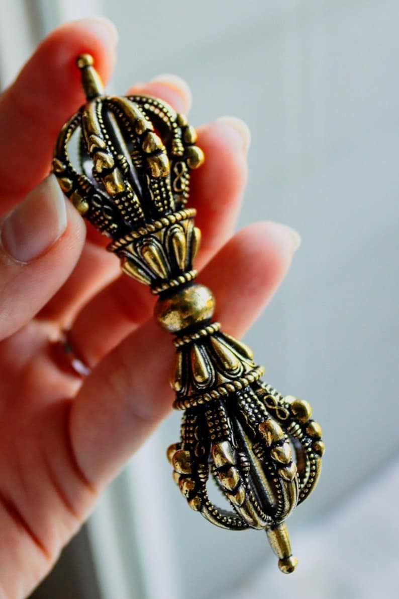 May include: A gold-colored metal hand-held prayer wheel with intricate details and a pointed tip.