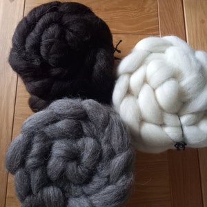 Könnte beinhalten: Drei Knäuel Wolle in Schwarz, Weiß und Grau. Die Wolle ist in einem Kreis auf einer Holzoberfläche angeordnet.