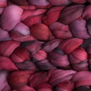 Könnte beinhalten: Nahaufnahme eines geflochtenen Textils in Rot-, Rosa- und Lilatönen. Das dicke, weiche Material ist in einem sich wiederholenden Muster angeordnet und erzeugt eine strukturierte Oberfläche. Die Farbpalette reicht von Hellrosa bis Dunkelburgunder.