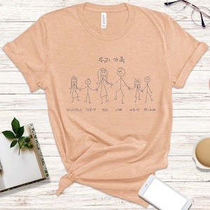 Peut inclure: Un t-shirt couleur pêche avec un motif de famille en bâtonnets. Le texte "우리 가족" est écrit au-dessus de la famille et les noms de chaque membre de la famille sont écrits en dessous. Les noms sont "나현/민지", "남동생", "엄마", "아빠", "여동생", "형/오빠".
