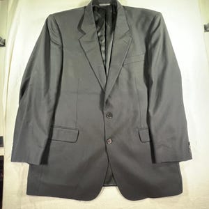 May include: A solid black blazer featuring a notched lapel, a two-button front closure, and two flap pockets at the waist. The garment includes long sleeves with buttoned cuffs and a smooth interior lining, presenting a structured silhouette.