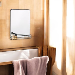 May include: A black framed mirror with a small shelf underneath. The shelf is holding several small bottles. The mirror is mounted on a wooden wall.