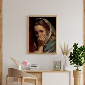 May include: A painting of a woman with a white headscarf covering her hair, she is crying and covering her mouth with her hand. The painting is framed in a wooden frame.