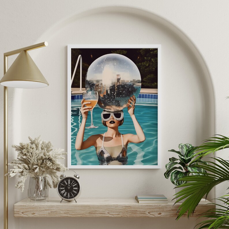 May include: A woman in a silver swimsuit and sunglasses holds a disco ball above her head while floating in a pool.