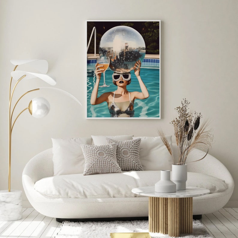 May include: A woman wearing sunglasses holds a disco ball above her head while floating in a swimming pool. The pool is surrounded by a wooden deck and lush greenery.