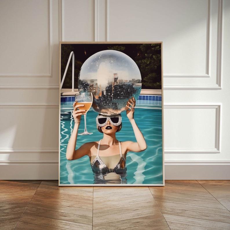 May include: A woman in a silver swimsuit and sunglasses holds a disco ball above her head while floating in a swimming pool.