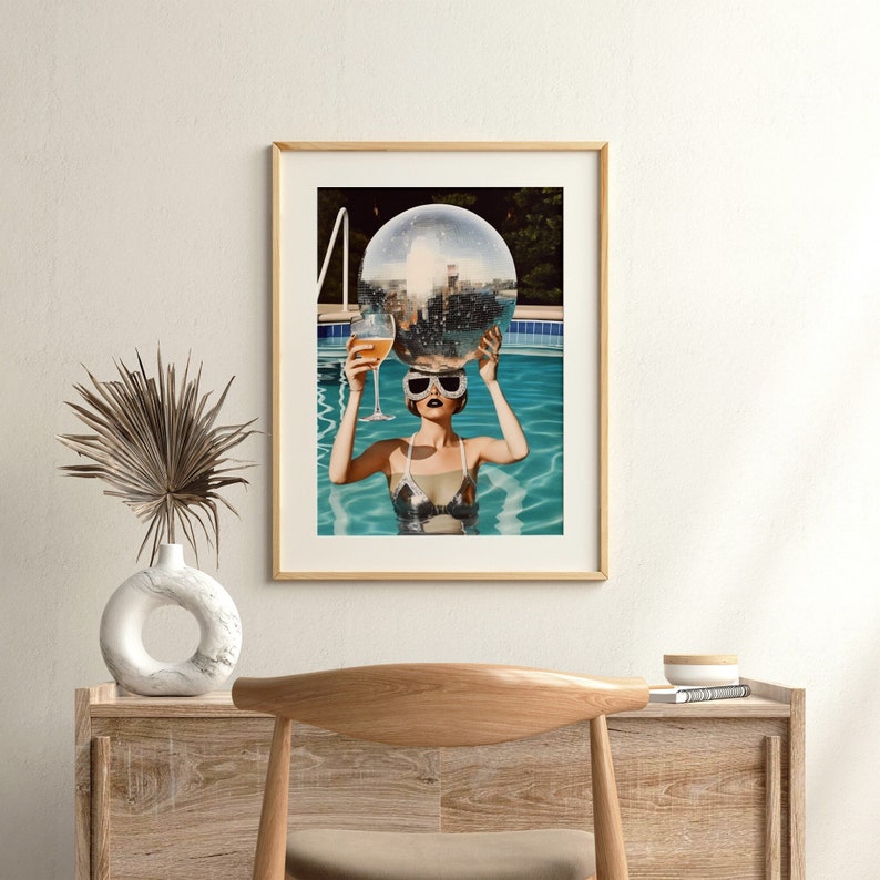 May include: A woman in a swimming pool wearing sunglasses and a silver swimsuit holds a disco ball above her head and a glass of wine in her other hand.