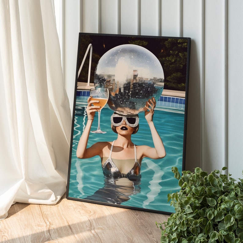 May include: A woman in a silver swimsuit and sunglasses holds a disco ball above her head while floating in a swimming pool.