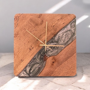 May include: Square wooden clock with a grey and silver resin inlay. The clock has gold hands and a simple design.