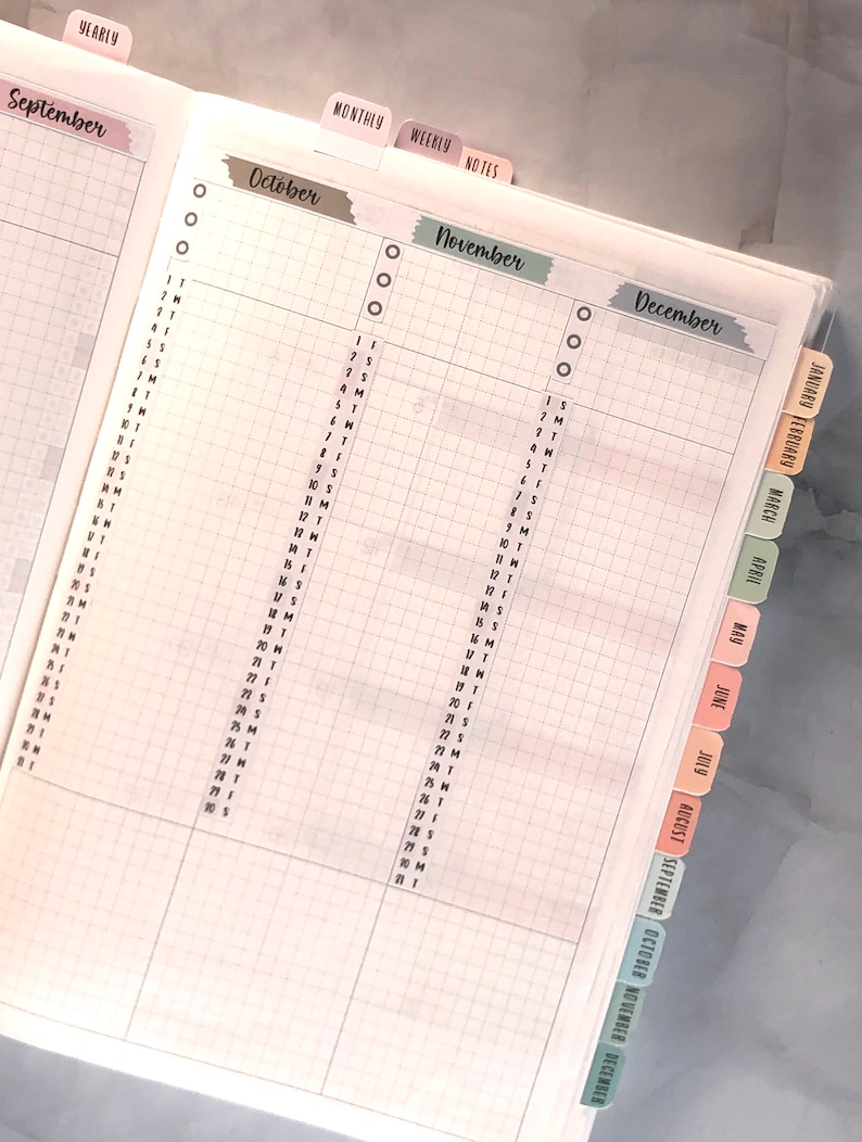 May include: A monthly planner with tabs for each month of the year, September through December. The tabs are color-coded and have the month name written on them.
