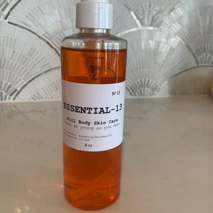 Peut inclure: Une bouteille transparente contenant un liquide orange. La bouteille est munie d'un bouchon pompe blanc et d'une étiquette blanche avec le texte "ESSENTIAL-13 Full Body Skin Care Look as young as you feel" et "8 oz".
