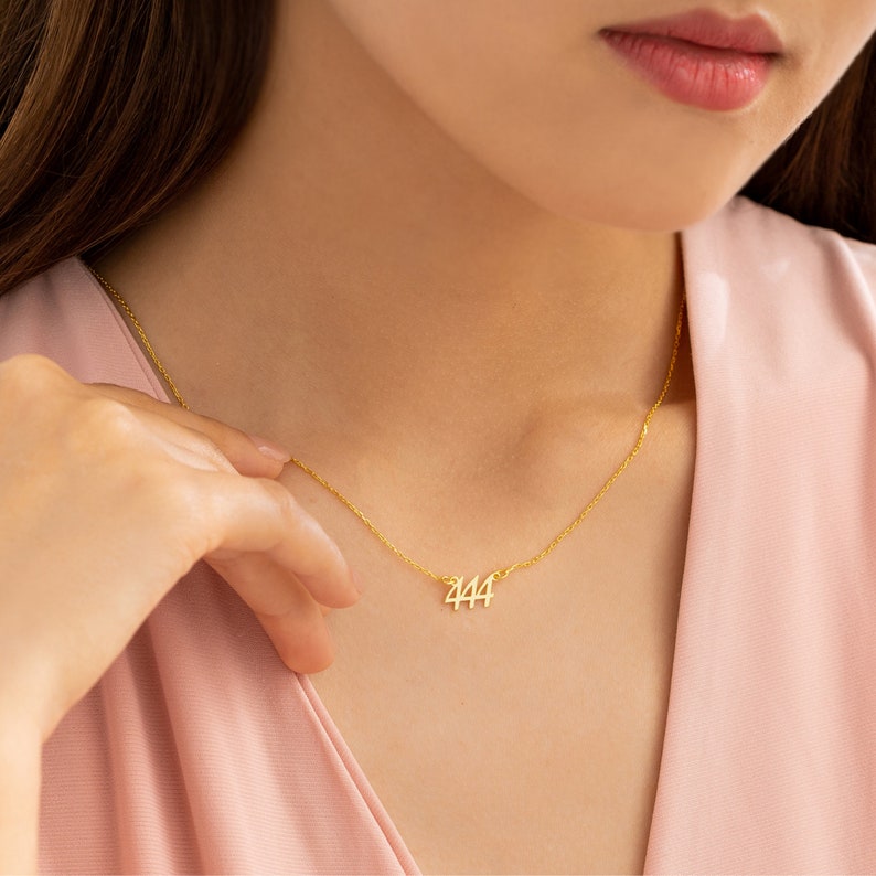 May include: A gold necklace with a delicate chain and a pendant featuring the number 444.
