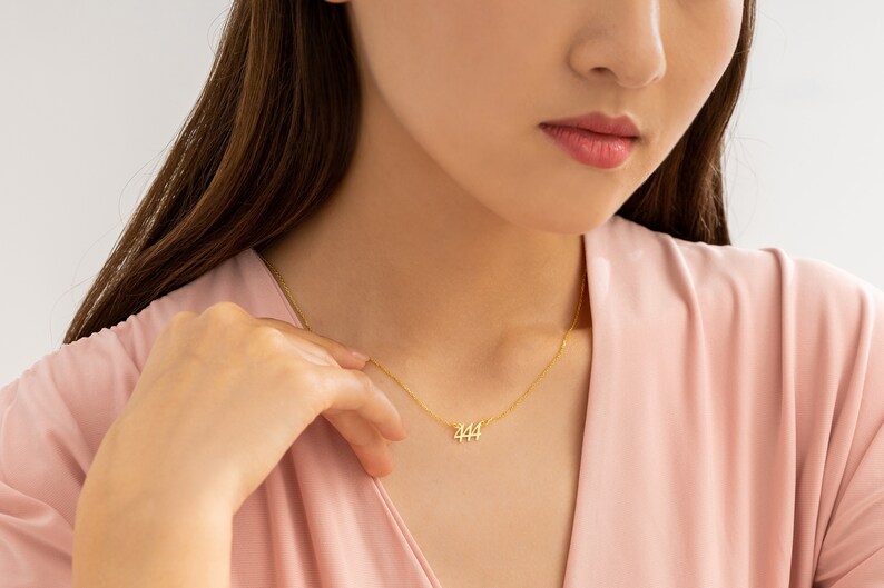 May include: A gold necklace with a delicate chain and a pendant featuring the number 444.