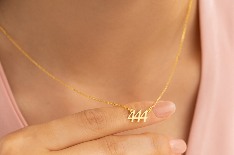 May include: A gold chain necklace with a pendant featuring the number 444.