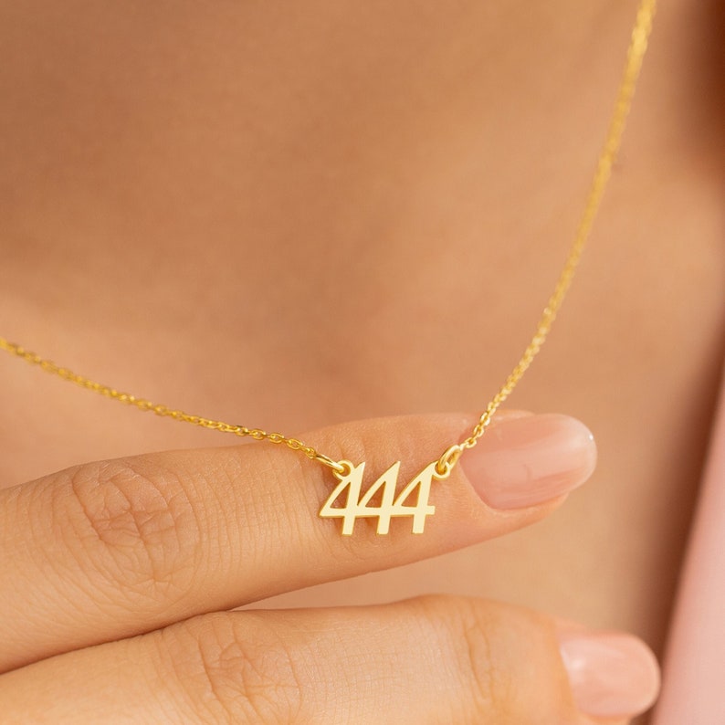 May include: A gold chain necklace with a pendant featuring the number 444.