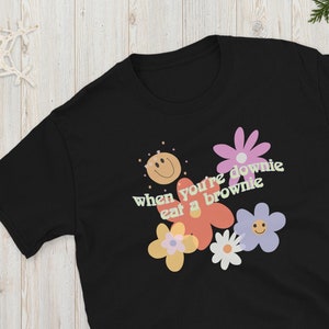 May include: Black t-shirt with a graphic of colourful flowers and the text "when you're downie eat a brownie".