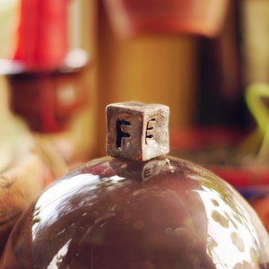 Peut inclure: Gros plan d'un petit objet cubique en argent avec la lettre "F" sur chaque face, posé sur un dôme en verre brun.