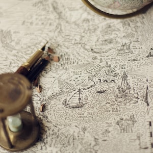 May include: A detailed map with a nautical theme, featuring a sailing ship, islands, and text. A brass hourglass, pencils, and a globe are arranged on the map. The map is hand-drawn with intricate lines and details.