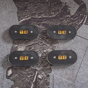 May include: Four black oval-shaped counter pieces with yellow numbers. The numbers are 18, 99, 21, and 37.