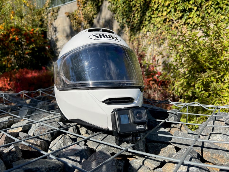 May include: White motorcycle helmet with a clear visor and a black GoPro camera attached to the front.