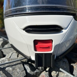 May include: White motorcycle helmet with a black visor and a red button on the back. The helmet is sitting on a gray metal grate.