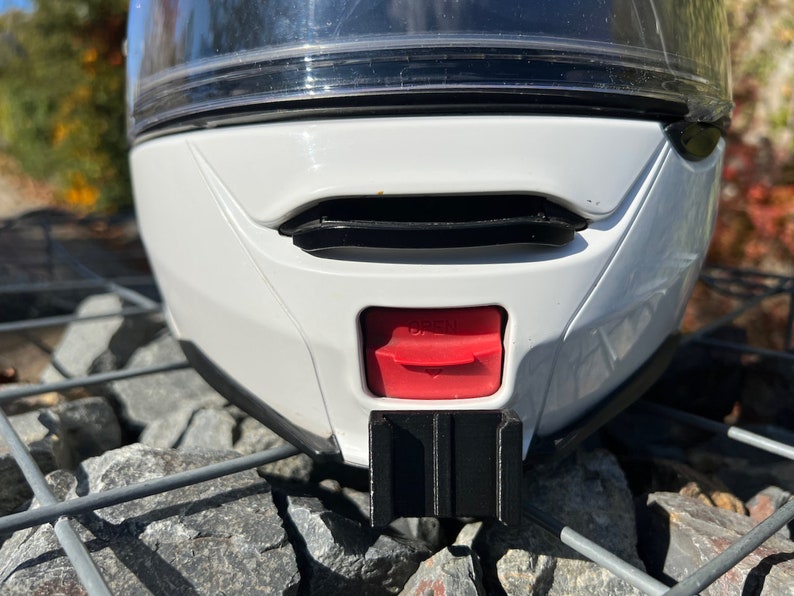 May include: White motorcycle helmet with a black visor and a red button on the back. The helmet is sitting on a gray metal grate.