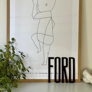 May include: A black and white line drawing of a baby in a frame with the name "FORD" in black block letters below the drawing. The text below the drawing reads "SCALE 1:1 OF JACKSON 5 INCHES / 7 POUNDS 12 OUNCES AU 14, 2018"