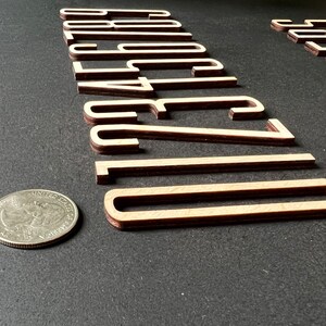 Puede incluir: N&uacute;meros de madera 0, 1, 2, 3, 4, 5, 6, 7, 8, 9 y 0, de color ligeramente marr&oacute;n rojizo, dispuestos en fila sobre una superficie negra.
