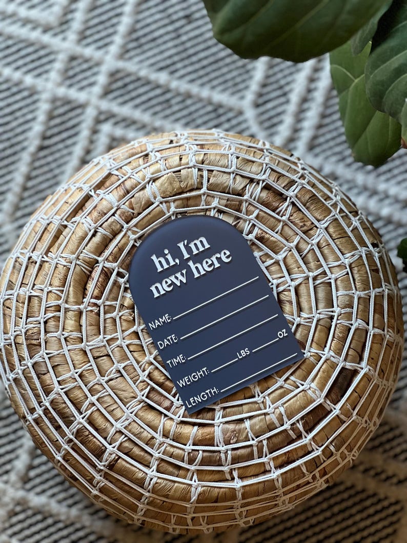May include: A navy blue birth announcement tag with the text "hi, I'm new here" in white. The tag includes spaces to write the baby's name, date, time, weight in pounds and ounces, and length.