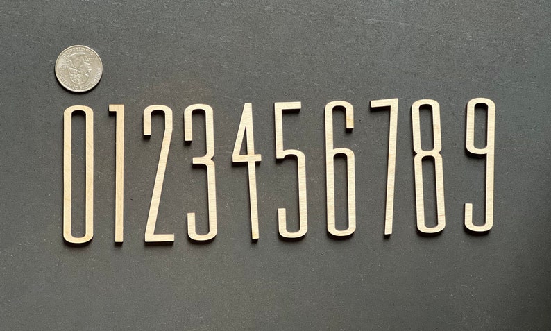 Puede incluir: Diez n&uacute;meros de madera, del 0 al 9, de color marr&oacute;n claro. Los n&uacute;meros est&aacute;n en una fuente sans-serif y tienen un borde ligeramente elevado.