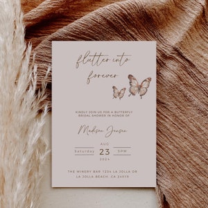 May include: A light grey invitation card with the text "flutter into forever" in brown script. The card features two watercolour butterflies in shades of brown and orange. The text "Kindly join us for a butterfly bridal shower in honour of Madison Jensen" is printed in brown. The date and time of the event are listed as "Saturday, August 23, 2024 at 5 PM". The location is listed as "The Winery Bar, 1234 La Jolla Dr, La Jolla Beach, CA 24019."