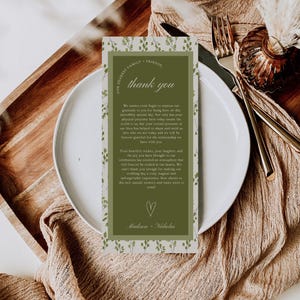 May include: A thank you card with a green border and floral accents. The card features the words "thank you" in elegant script, along with a heartfelt message. The names "Madison + Nicholas" are at the bottom.