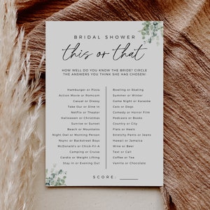 Peut inclure: Une carte blanche avec un feuillage vert en bas et le texte "Bridal Shower this or that" en haut. La carte contient une liste de 16 questions "à la fois ou à l'autre" pour un jeu de douche nuptiale. Les questions incluent "Hamburger ou Pizza", "Film d'action ou comédie romantique", "Décontracté ou habillé", "Prendre à emporter ou dîner sur place", "Netflix ou théâtre", "Halloween ou Noël", "Lever du soleil ou coucher de soleil", "Plage ou montagne", "Hibou de nuit ou personne du matin", "Nsync ou Backstreet Boys", "McDonald's ou Chick-Fil-A", "Camping ou croisière", "Cardio ou musculation", "Rester à la maison ou sortir le soir", "Bowling ou patinage", "Été ou hiver", "Soirée jeux ou karaoké", "Chats ou chiens", "Comédie ou film d'horreur", "Podcasts ou livres", "Campagne ou ville", "Ballerines ou talons", "Pantalons amples ou jeans", "Hawaï ou Jamaïque", "Vin ou bière", "SMS ou appel", "Café ou thé", "Vanille ou chocolat". La carte comporte également le mot "SCORE:" en bas.