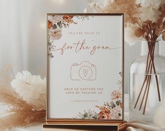 May include: A framed sign with the text "PLEASE SNAP IT for the gram" and a camera graphic with a heart. The sign is in a gold frame and stand, decorated with floral accents. The text "HELP US CAPTURE THE LOVE BY TAGGING US" is also included.