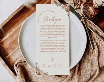 May include: A wedding thank you card with floral decorations and the words "thank you" in elegant script. The card is on a white plate with cutlery, and a wooden tray is in the background. The card includes a heartfelt message.