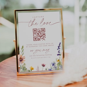 Könnte beinhalten: Ein weißes Schild mit goldenem Rahmen und floralen Akzenten. Das Schild sagt "Capture the love" und hat einen QR-Code. Es sagt auch "Teilen Sie Ihre Fotos mit uns, indem Sie den Code oben scannen oder Sie können den folgenden Hashtag verwenden #jensenwedding"