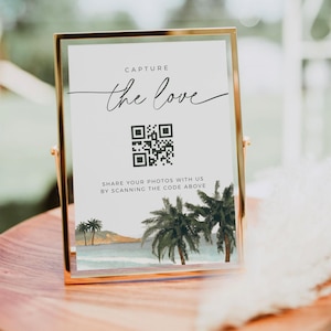 May include: A gold-framed sign with a white background and the text "Capture the love" in black. A black and white QR code is below the text with the words "Share your photos with us by scanning the code above". The bottom of the sign features a watercolor illustration of palm trees and a beach.