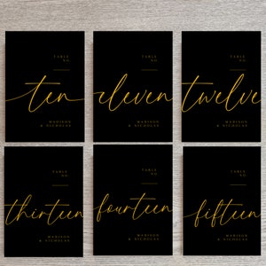 May include: Ten table cards with black backgrounds and gold text. The numbers ten through fifteen are written in cursive script. Each card also includes the text "Table No." and "Madison & Nicholas".