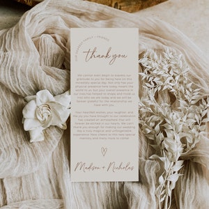 May include: A thank you card with a simple design in beige and brown tones. The card features the text "Thank You" in a script font and the names "Madison + Nicholas" at the bottom. The card is surrounded by a delicate white fabric.