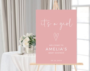 May include: Pink welcome sign with white text that reads "it's a girl" with a small heart and the text "Welcome to Amelia's Baby Shower 08.25.20XX".