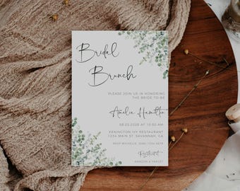 May include: A light gray bridal shower invitation with a watercolor design of green leaves and the text "Bridal Brunch" in black script. The invitation includes the bride-to-be's name, "Amelia Hamilton", the date and time of the event, the location, and RSVP information. The text "Registered at Amazon & Target" is also included.