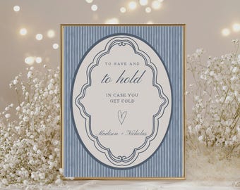 May include: A framed sign with the text "TO HAVE AND to hold IN CASE YOU GET COLD" in a decorative oval. The background is blue with vertical stripes. The names "Madison + Nicholas" are at the bottom, with a heart symbol.