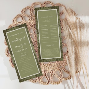 Puede incluir: Dos programas de boda con fondos verde oliva y bordes blancos se muestran en un salvamanteles tejido. Los programas presentan el texto "Welcome to the wedding of Madison and Nicholas" y "Wedding Party". Hierba de la pampa seca en el fondo.